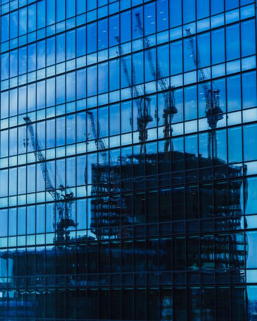 A low-angle view of modern high-rise office buildings in an urban environment, featuring glass curtain walls with reflective surfaces and grid-like window arrangements. The building on the right has a